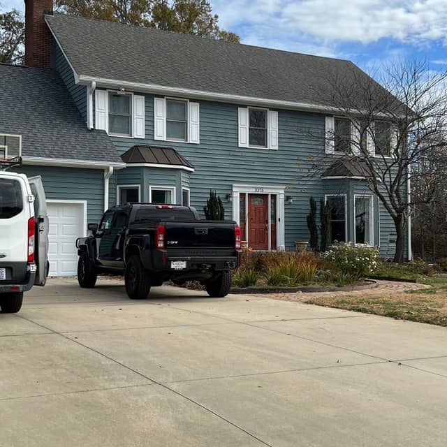 Two-storey blue-grey home with white trim and a red front door after an exterior repaint