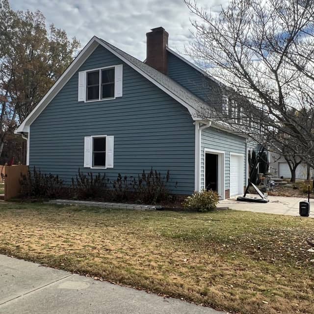 Freshly painted blue-grey lap siding on a gabled home with white window trim and a brick chimney