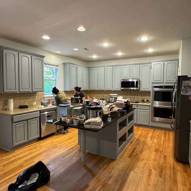 Kitchen part-way through a cabinet repaint, with grey-blue cabinet doors and the crew at work