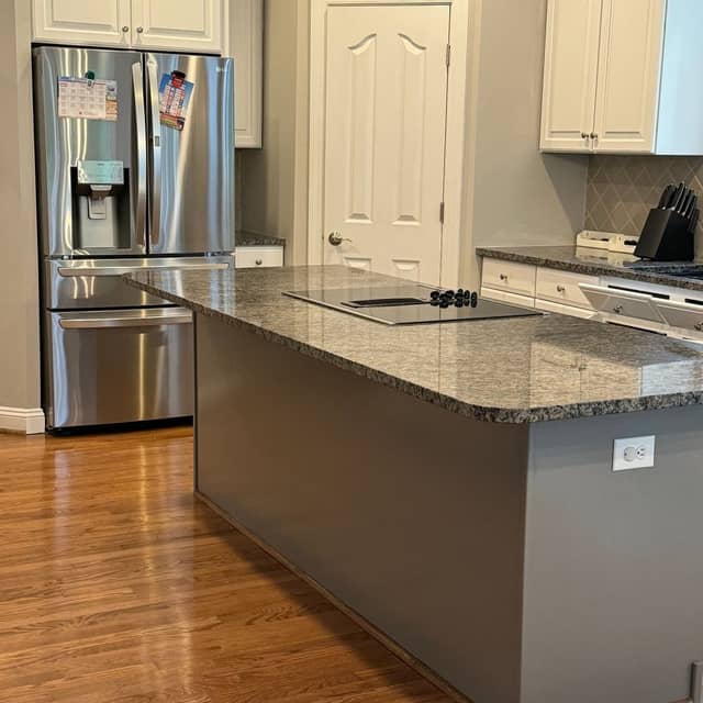 Kitchen with white painted cabinets and a grey painted island beside a stainless steel refrigerator