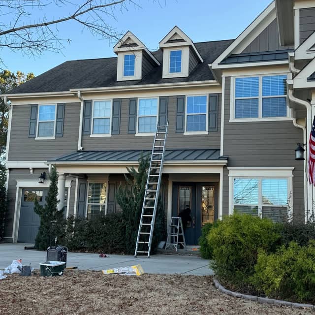 Two-storey home mid-repaint with an extension ladder against the front elevation and drop cloths laid out on the drive