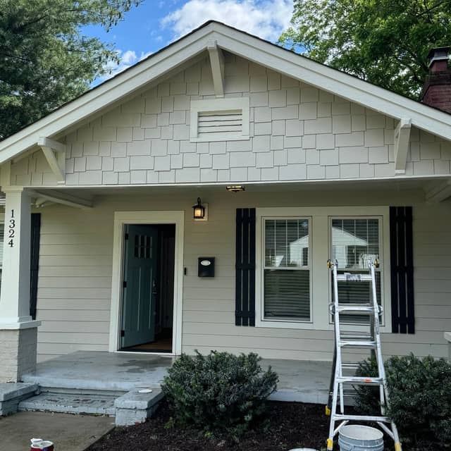 White bungalow with a dark green front door and a stepladder set up on the path during exterior work